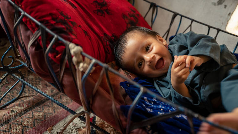 Arfanullah liegt in seinem Kinderbettchen und lacht fröhlich