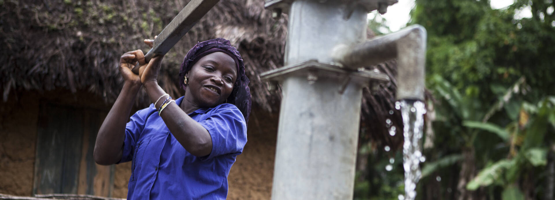 Frau in Sierra Leone betätigt Wasserpumpe.