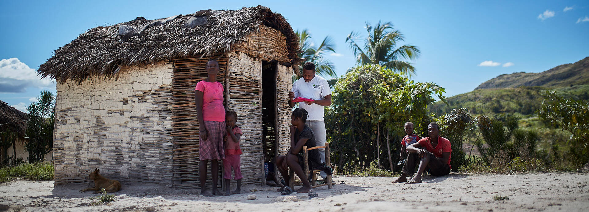 Ein Mitarbeiter von Aktion gegen den Hunger spricht vor einer kleinen Hütte mit einer Familie aus Haiti.