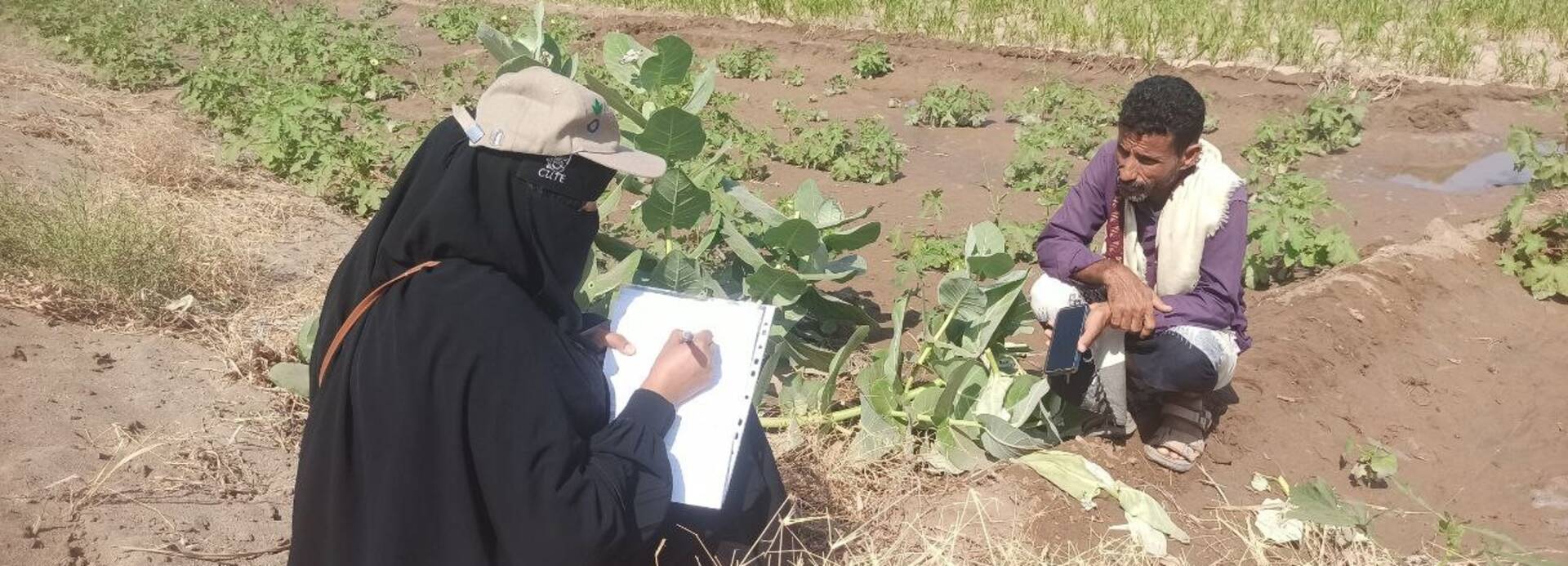 Eine Mitarbeiterin von Aktion gegen den Hunger spricht auf dem Feld mit einem Bauern und macht sich Notizen.