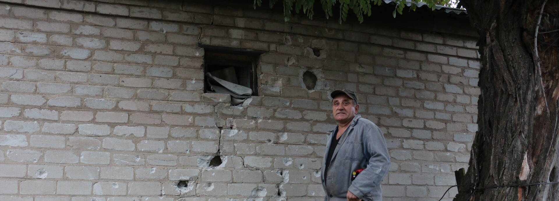 Ein Hilfeempfänger in der Ukraine steht vor einer zerschossenen Wand.