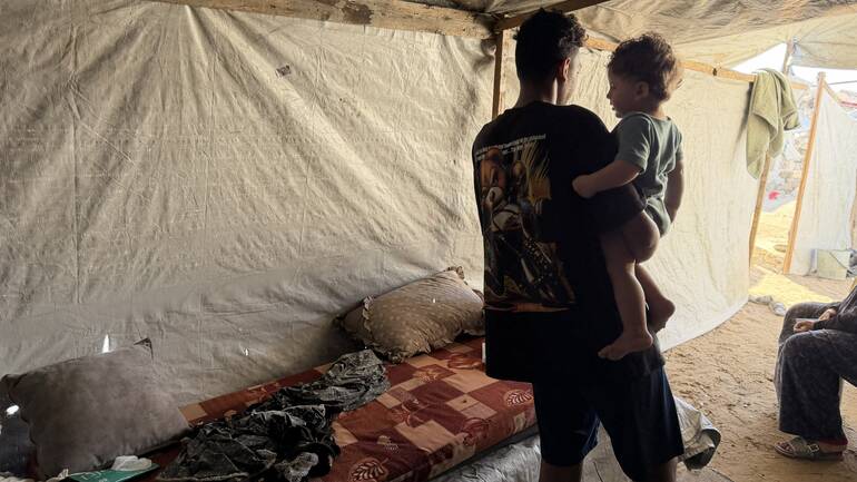 Ein älterer Junge mit seinem kleinen Geschwisterchen auf dem Arm im Zelt der Familie in Gaza