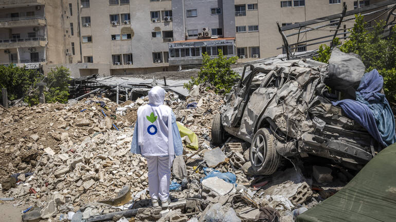 Mitarbeiterin von Aktion gegen den Hunger Libanon steht neben zerstörten Gebäuden und Auto