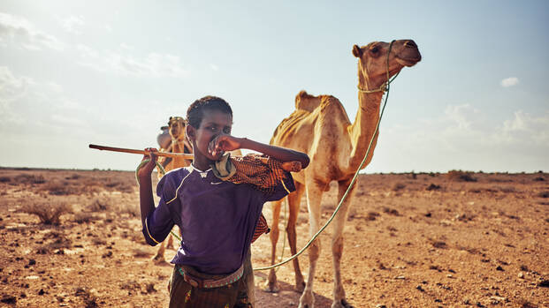 Junge in Somalia steht mit seinem Kamel in der Wüste.