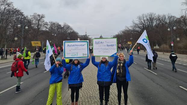 Vier Mitarbeiterinnen von Aktion gegen den Hunger halten im Januar 2023 Demoschilder und Flaggen auf der "Wir haben es satt!"-Demo hoch.