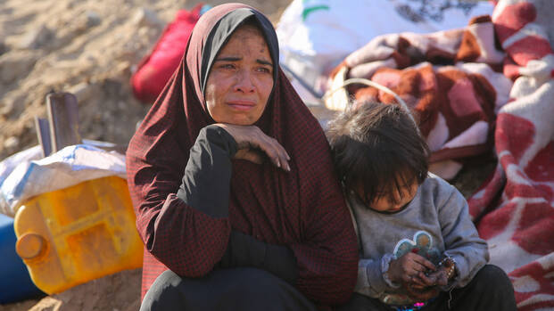 Eine Frau und ein Kind sitzen auf Decken im zerstörten Gazastreifen